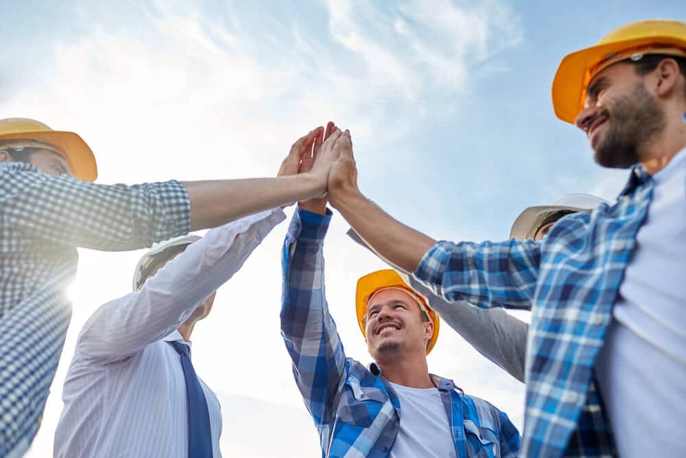 Five Smartway Builders workers in hard hats in a circle, high fiving to celebrate a positive outcome.